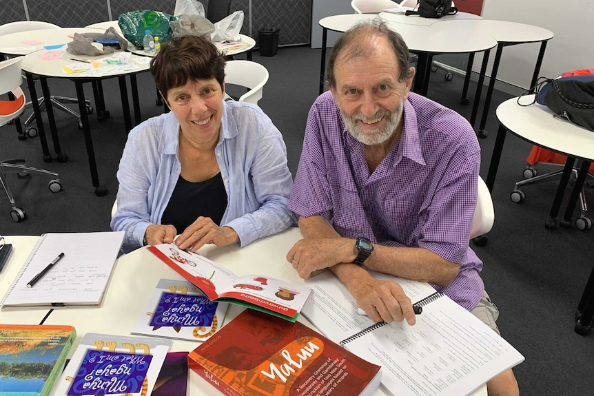 A woman and man sitting at a table with books on it.