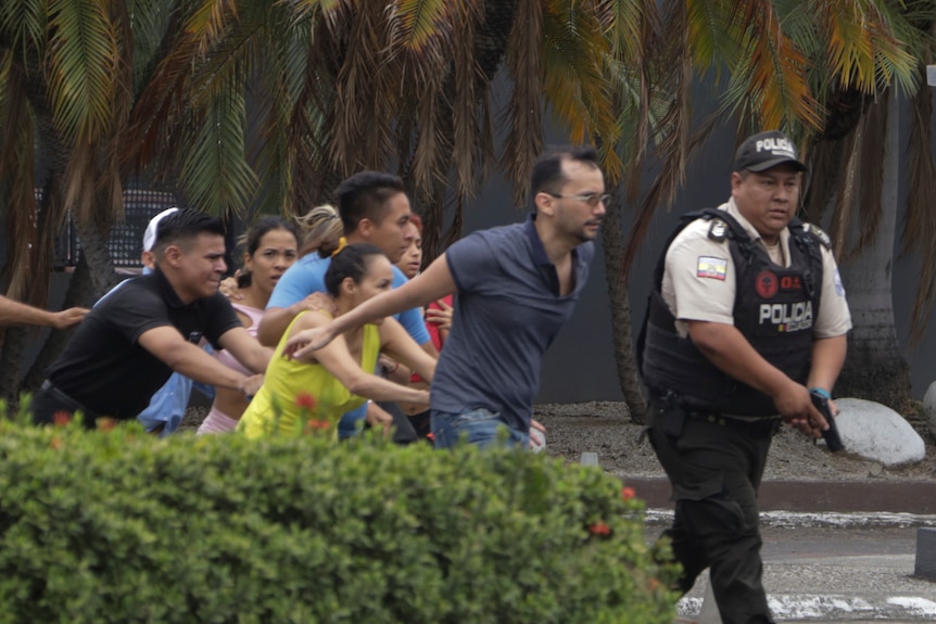People run behind a poliece officer holding a gun 