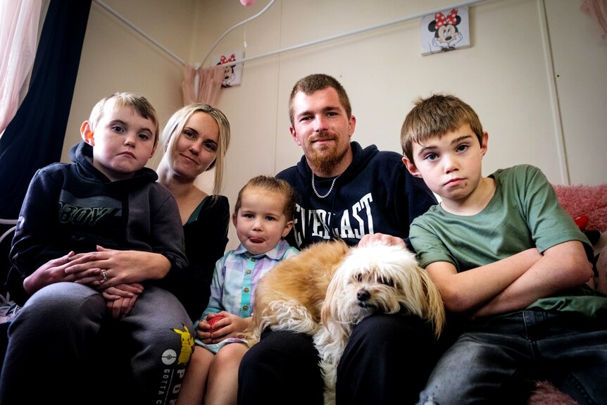 A family of five sits on a couch with a pet dog
