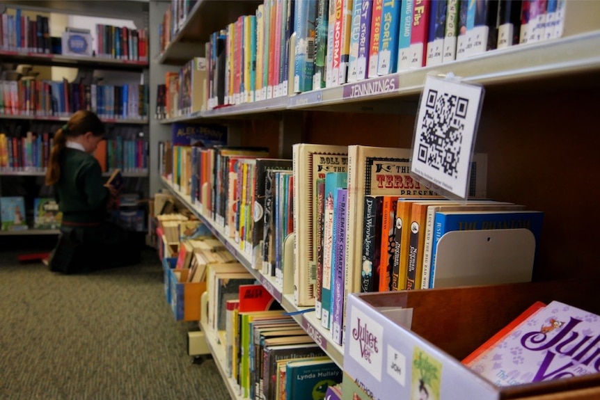 Three students sitting around a table in a school library reading books.