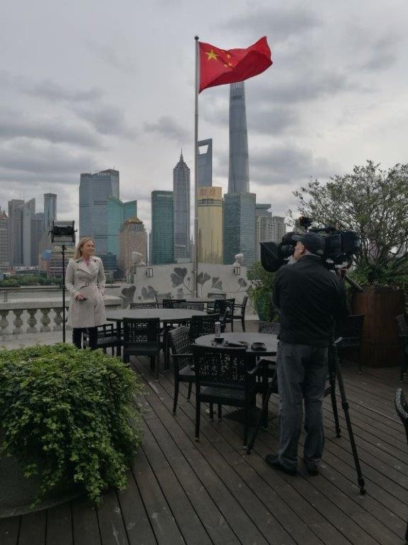 Pip Courtney being filmed by cameraman with Chinese flag and skyline in background.