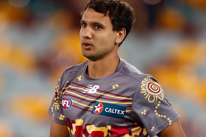 Callum Ah Chee holds a football while wearing the Brisbane Lions Indigenous training shirt