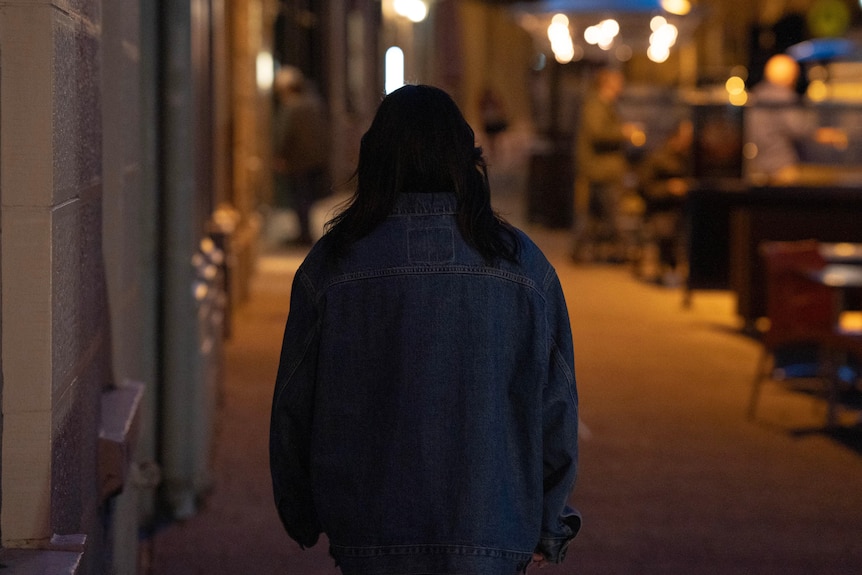 Woman wearing a denim jacket walking down a city street at night.