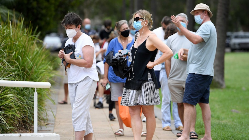 Women and men wearing face masks standing in line outside.