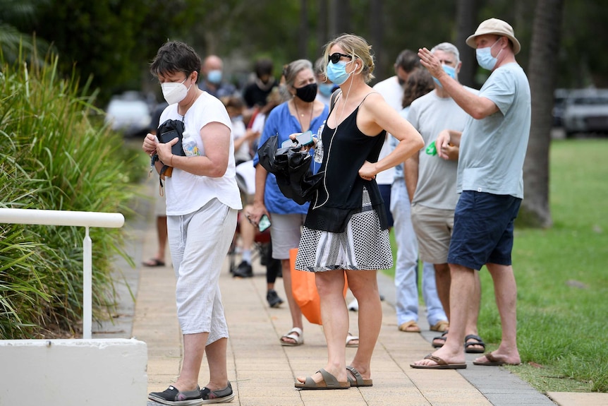 Women and men wearing face masks standing in line outside.