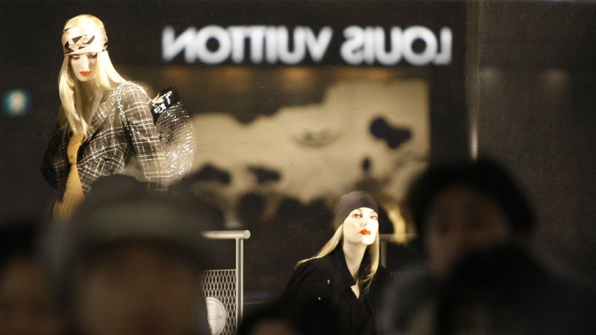 Passersby walk past a display window as the logo of Louis Vuitton is reflected on it