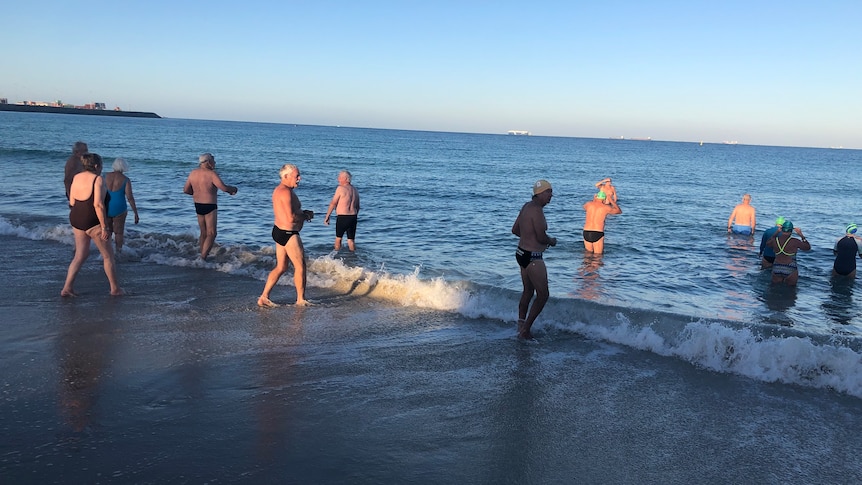 A wide shot of swimmers entering the water at Port Beach.