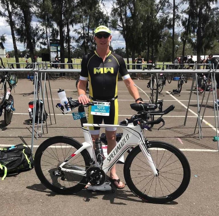 A man in cycling gear standing next to a bike, during a triathlon event.