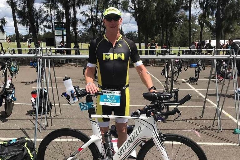 A man in cycling gear standing next to a bike, during a triathlon event.