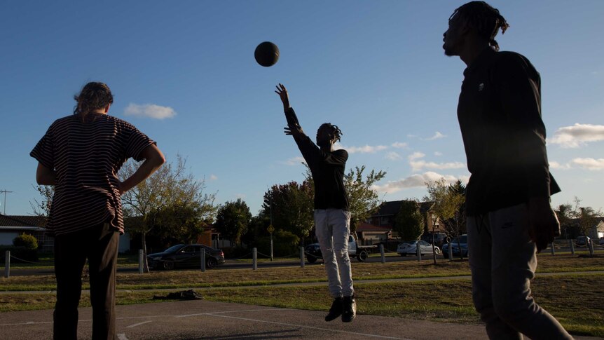 A silhouette of Mohamed playing basketball with two other boys.
