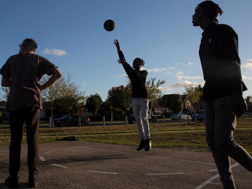 A silhouette of Mohamed playing basketball with two other boys.