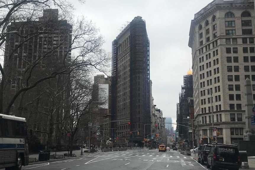 A nearly empty street in New York surrounded by buildings and trees.