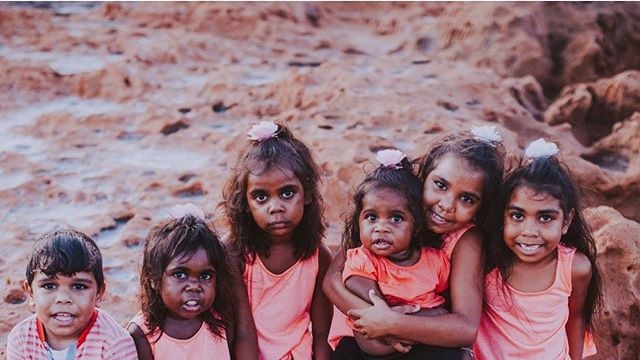 A group of indigenous Australian children smile at the camera.