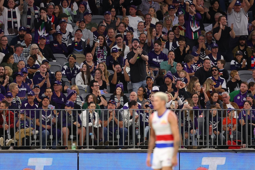 Fremantle Dockers fans shout at Western Bulldogs AFL player Rory Lobb, blurry in the foreground, during a game.