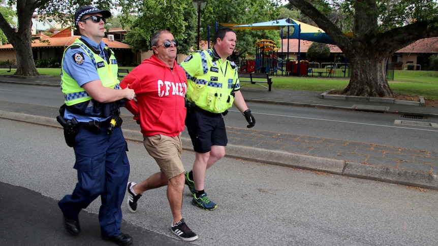 A man wearing a CFMEU sweater is flanked by two police officers and marched down a street.