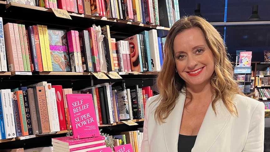 Tory Archbold wearing a white blazer standing next to pink books at a book store