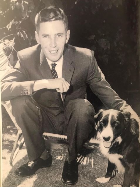 A man in a suit sitting on the ground next to a dog. 