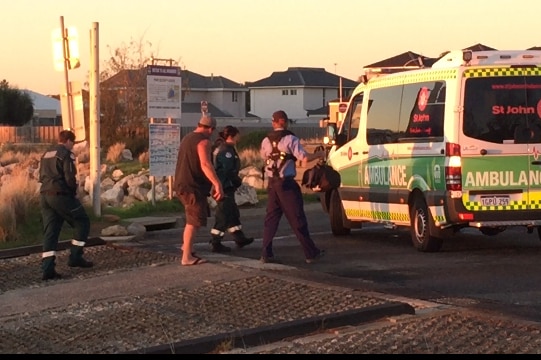 Man walks to ambulance escorted by paramedics and a police officer.