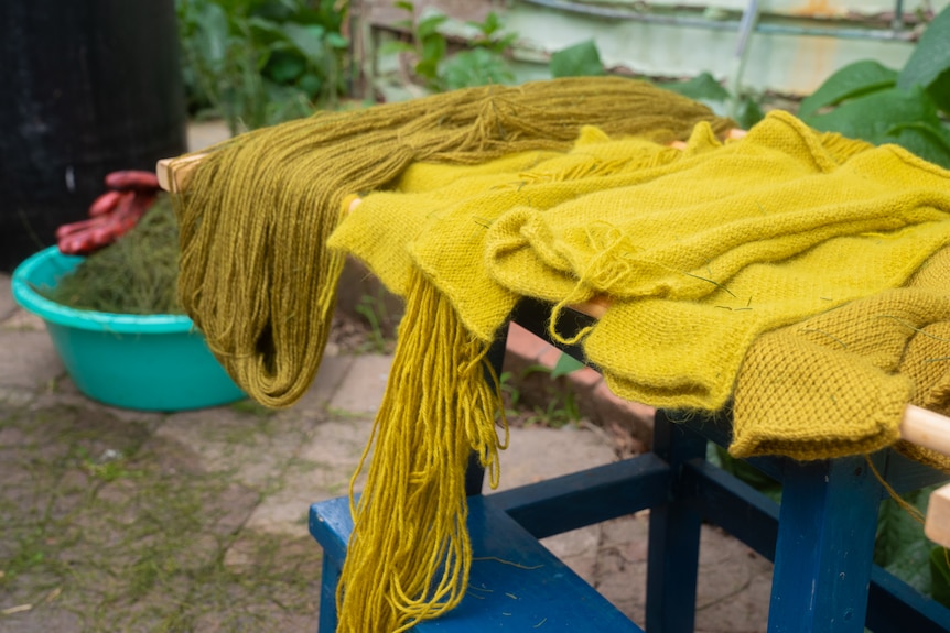 Items of different shades of light yellow clothing are seen on a blue painted wooden table in a garden.