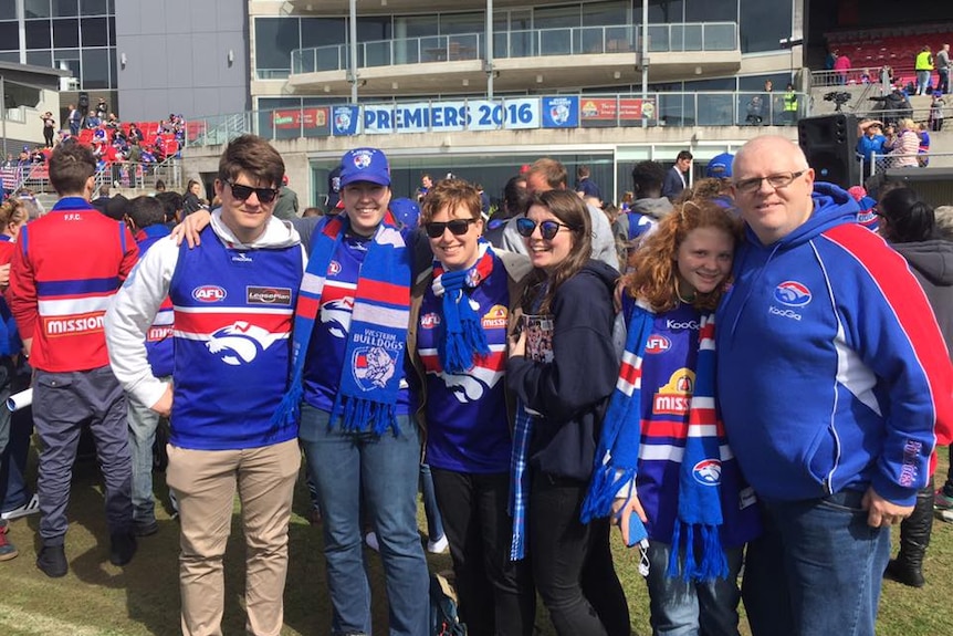 Kate O'Halloran wears a Western Bulldogs scarf and guernsey while standing in from of a banner that says "Premiers 2016".