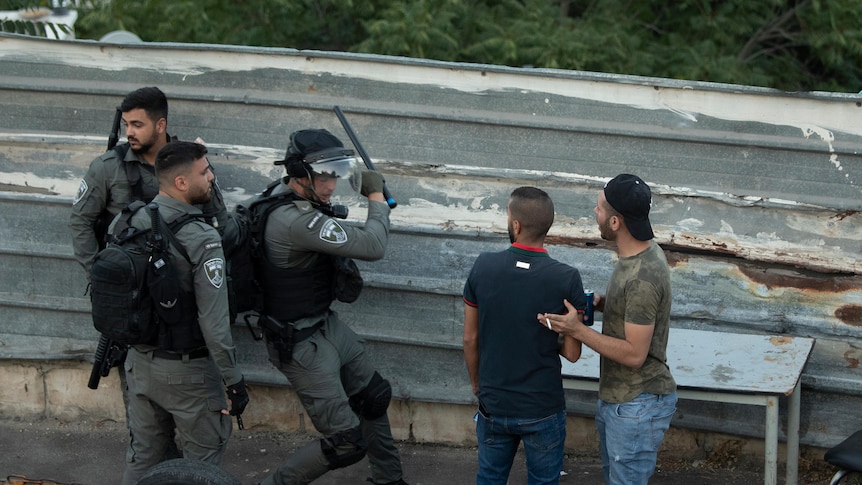 An Israeli border police officer prepares to hit a Palestinian man.