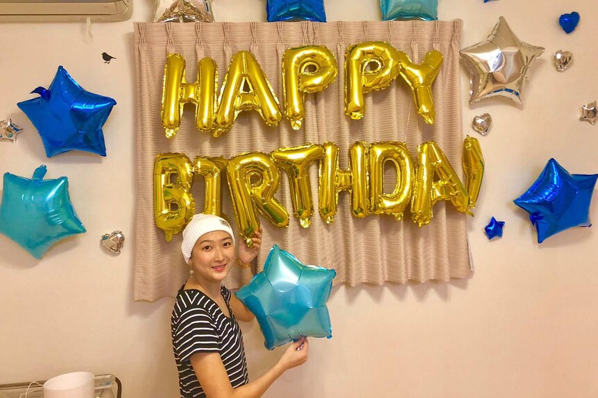 Rikako Ikee smiles while holding a star balloon in front of balloons spelling out "HAPPY BIRTHDAY". She has a bandaged head.