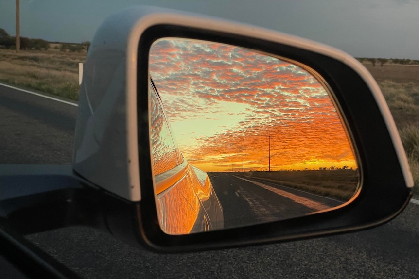 An orange sunset reflected out of the rearview mirror of a car