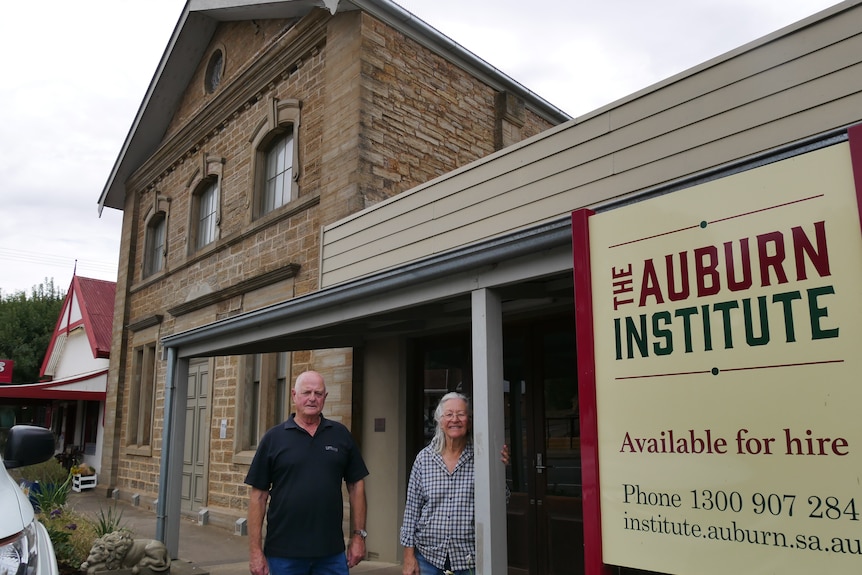 A man and woman stand outside Auburn Institute on the town's main street, with the hall's sign in the foreground. 