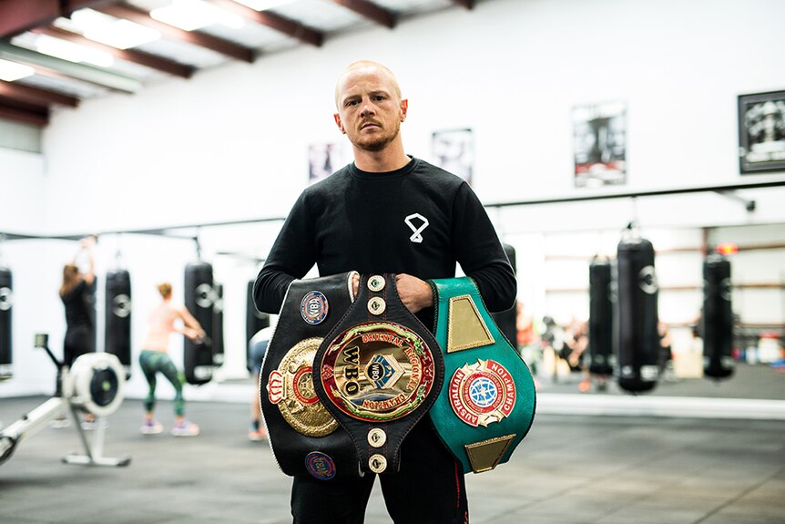 A man holding three boxing title belts.