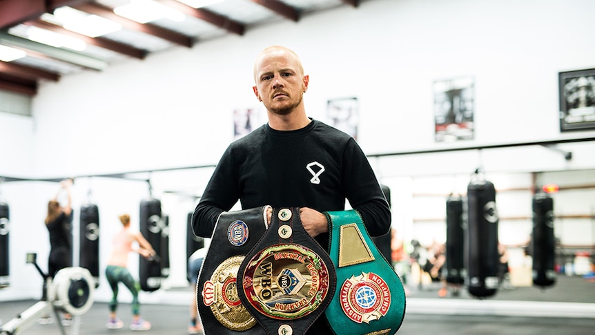 A man holding three boxing title belts.