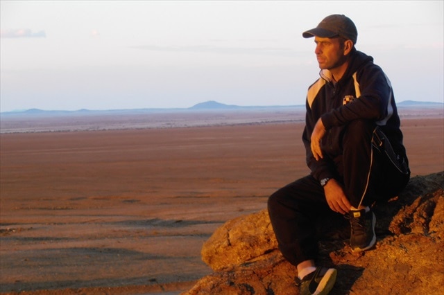 Matt Napier looking out to horizon, sitting on a rock in the African desert.