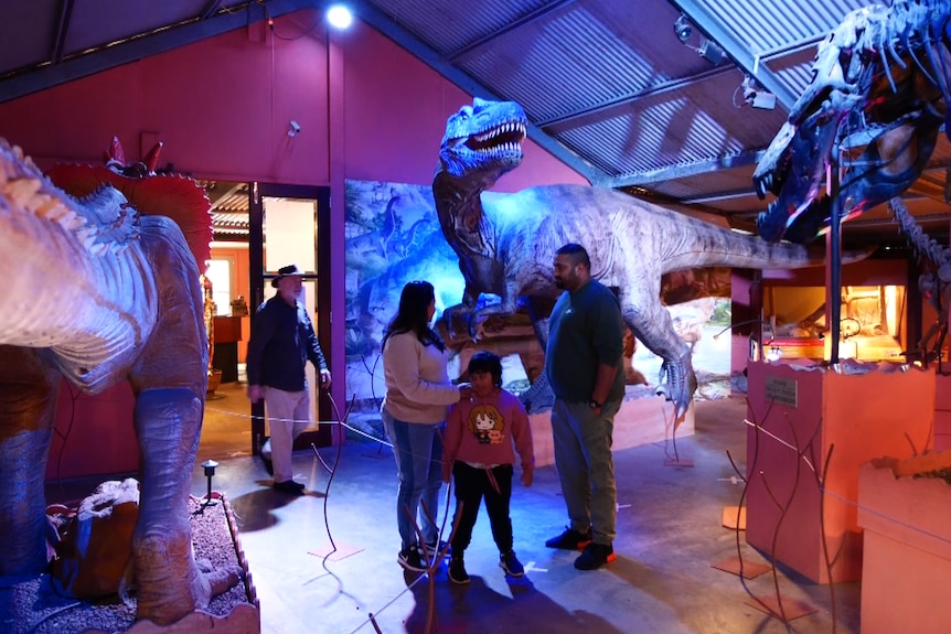 A family of three stand next to life-like dinosaur sculptures in an exhibition space.