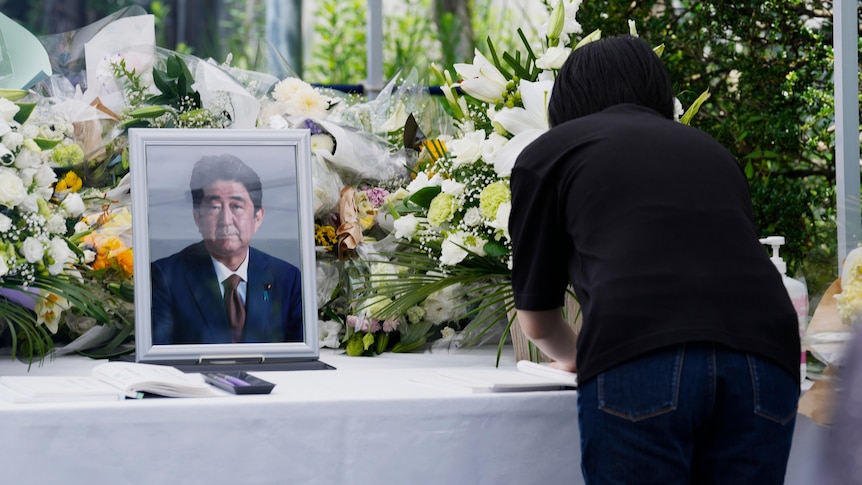 A woman writes in book next to framed photoraph of Mr Abe