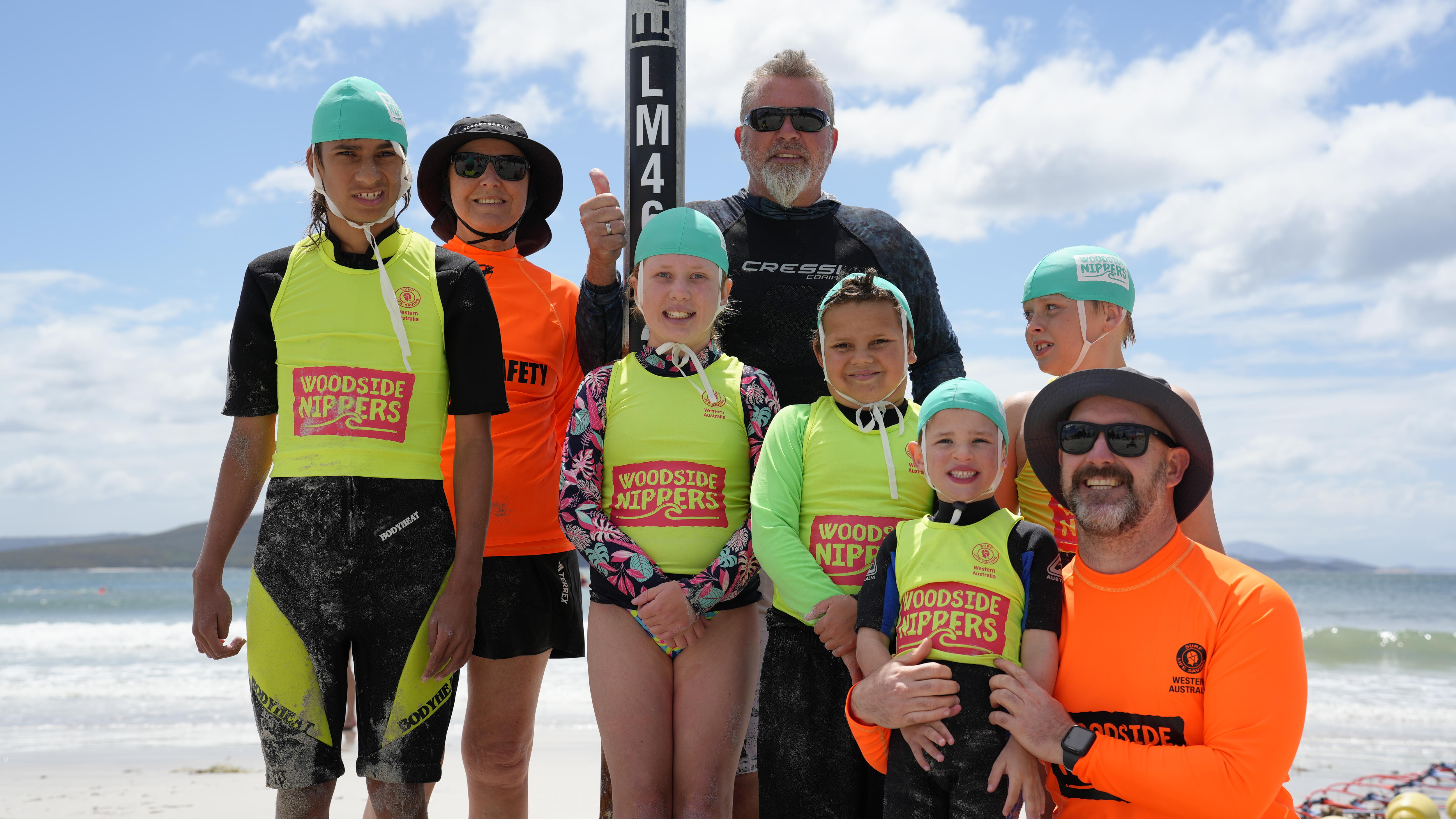 Cinco niños en uniforme de alicates con tres adultos en un grupo en la playa