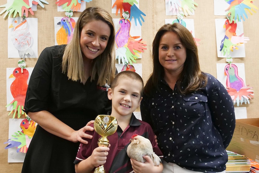 Two female teachers standing with child and chicken.