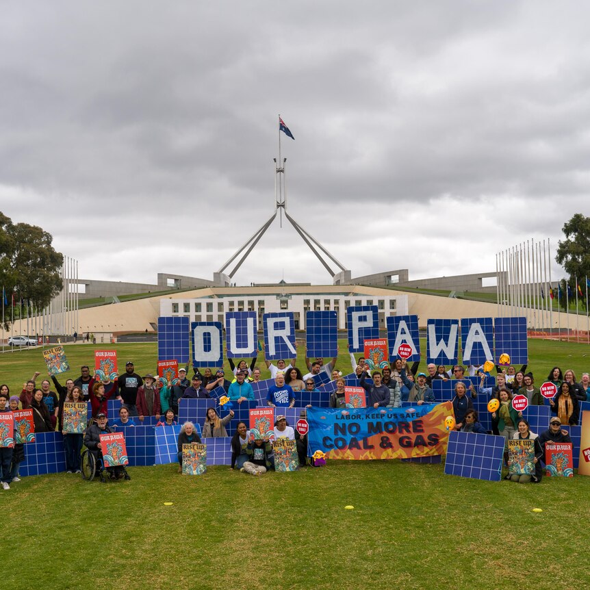 A group of climate activists with signs on the lawn of the Australian Parliament House in Canberra