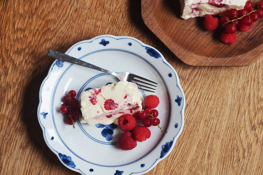 A slice of raspberry and creme fraiche semifreddo on a plate with a side of raspberries and red currants.