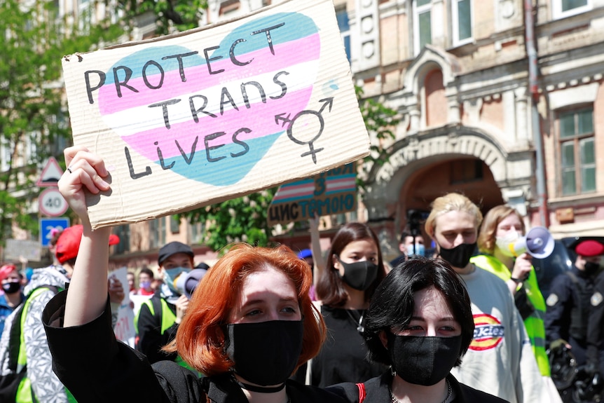 A group of activists march for trans rights, one holds a sign saying "protect trans lives". 