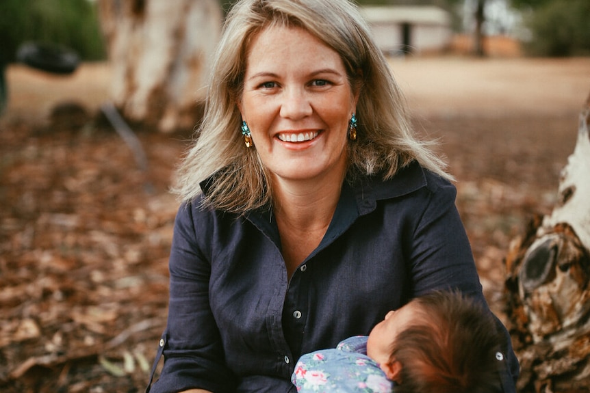 woman with a baby sitting in a field of autumn leaves