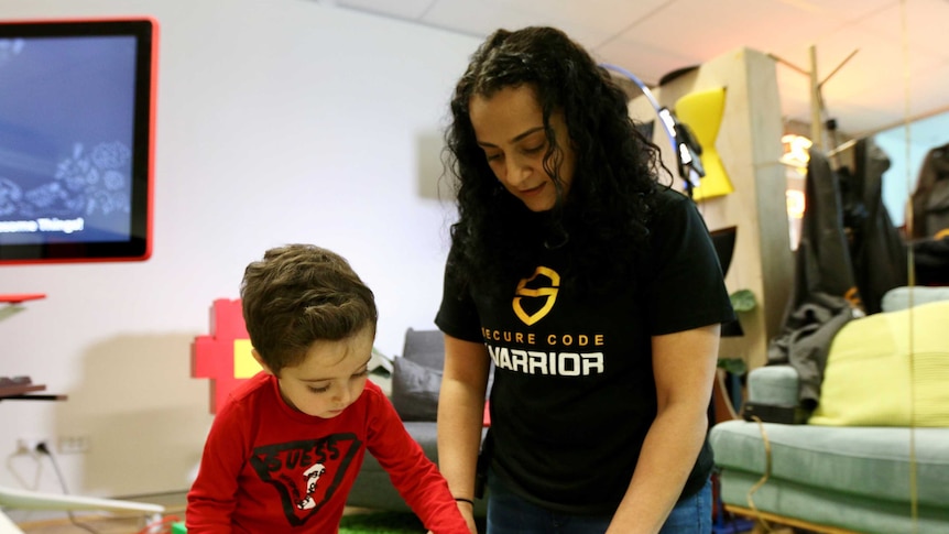 A woman kneels on the floor beside her son as he picks a coloured pen.