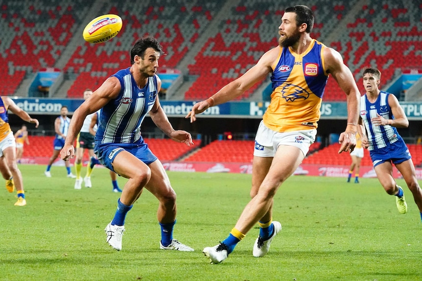 West Coast forward Josh Kennedy kicks the ball as North Melbourne's Robbie Tarrant looks on.