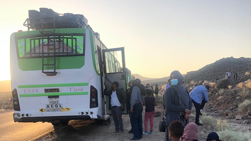 A green bus sits on the side of the road in an arid part of Ethiopia as passengers wait