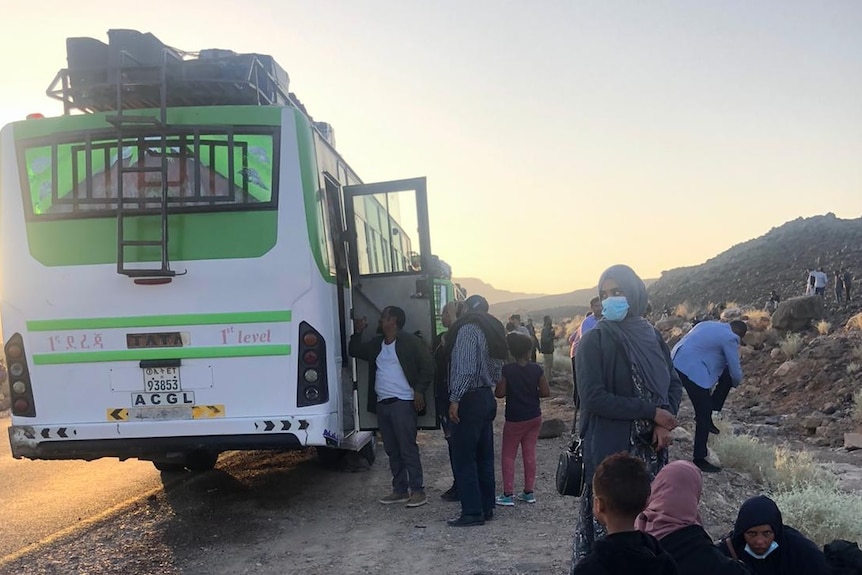 A green bus sits on the side of the road in an arid part of Ethiopia as passengers wait