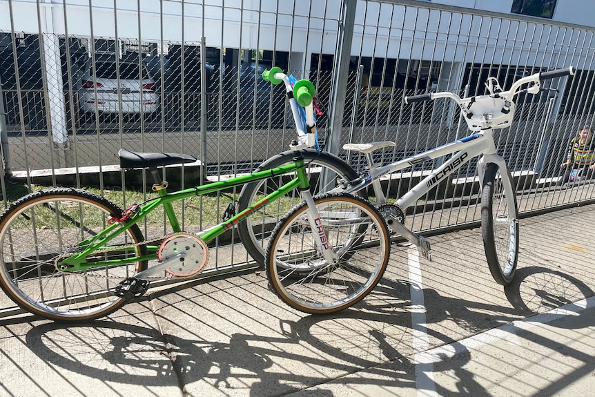 An older BMX bike and a new one leaning against a fence.