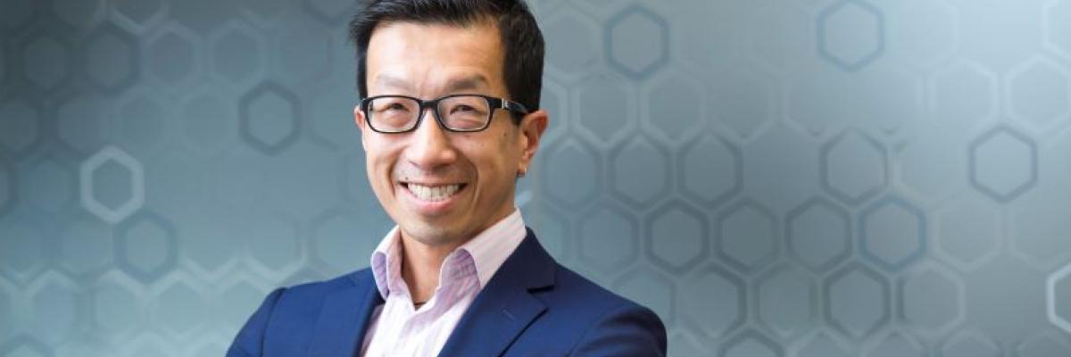 Man in blue suit and glasses stands in front of hexagonal background 
