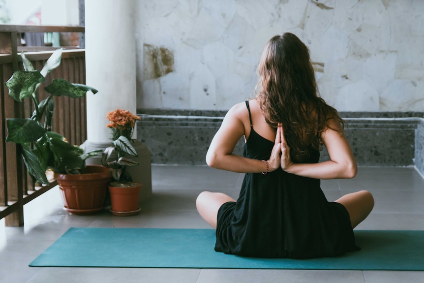 A woman sits on a yoga mat while holding her hands, for a story on online exercise programs.