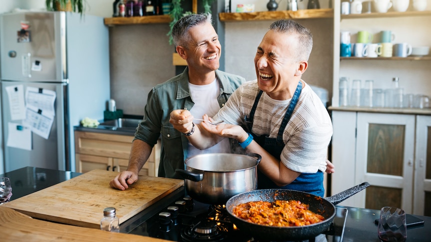 Cheerful gay couple talking and laughing while cooking in a kitchen