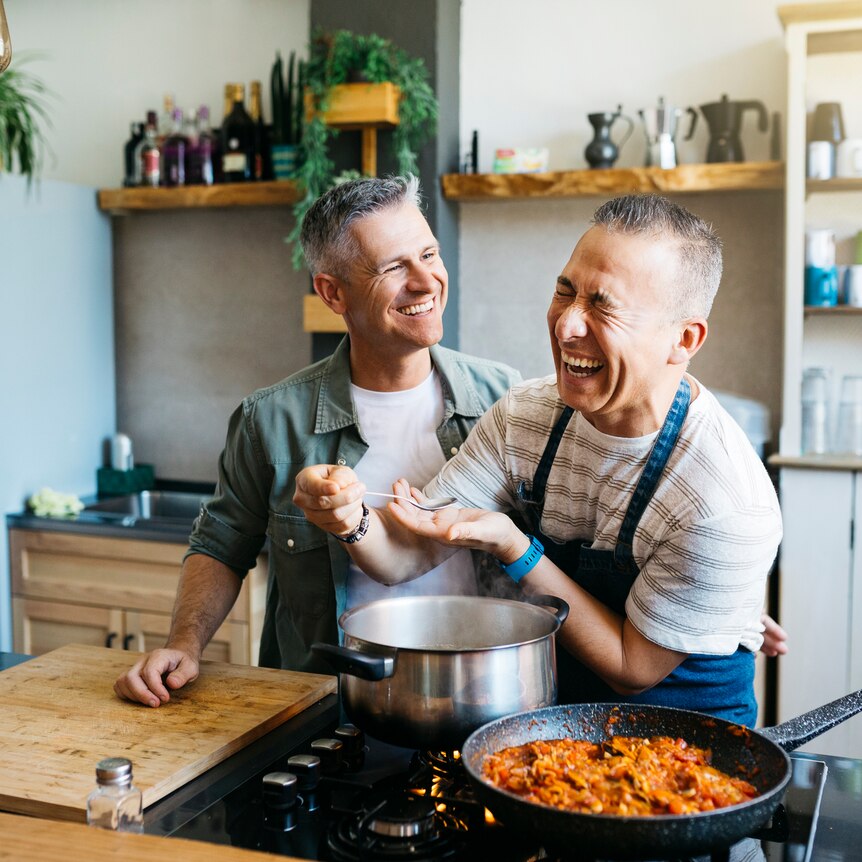 Cheerful gay couple talking and laughing while cooking in a kitchen