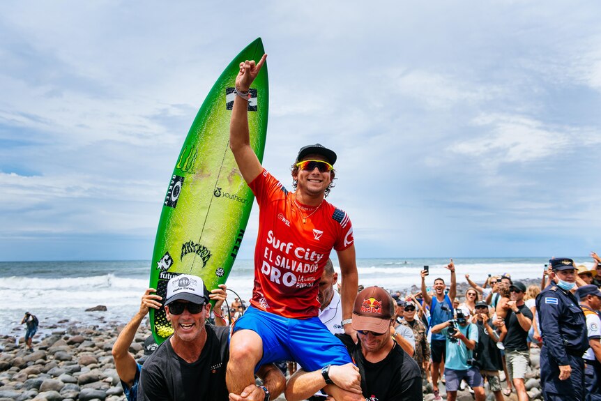 A male surfer is held up on the shoulders of friends after winning a competition