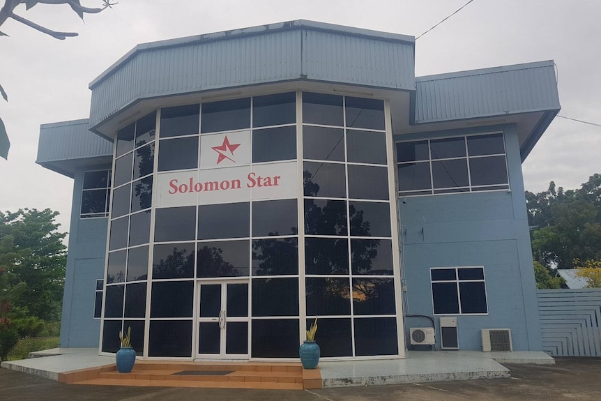 A blue grey building with black windows across the front and a sign reading: "Solomon Star".